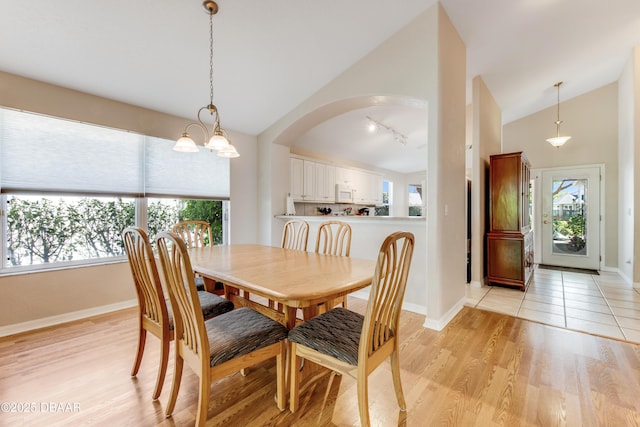 dining space with light wood-type flooring, track lighting, arched walkways, baseboards, and vaulted ceiling