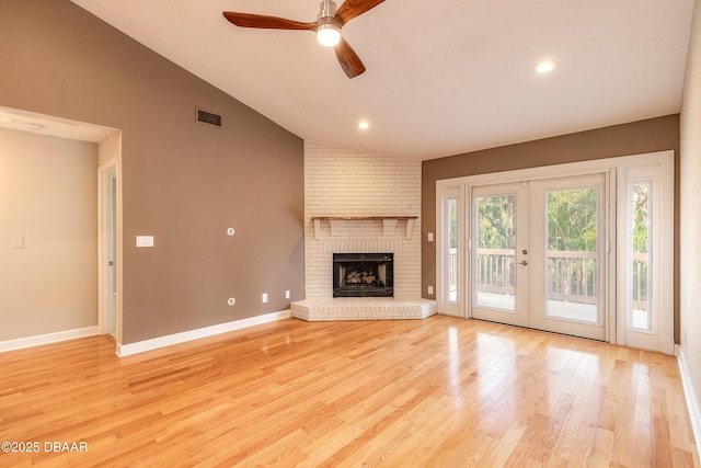 unfurnished living room featuring french doors, lofted ceiling, ceiling fan, light wood-type flooring, and a brick fireplace