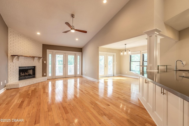 unfurnished living room with light hardwood / wood-style flooring, french doors, ceiling fan, sink, and ornate columns