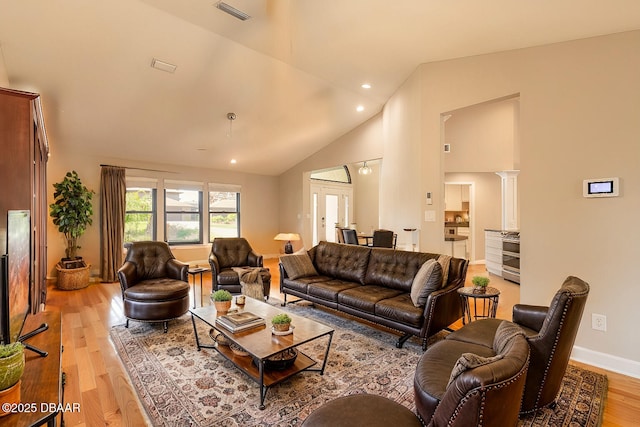 living room featuring light hardwood / wood-style floors, high vaulted ceiling, and decorative columns