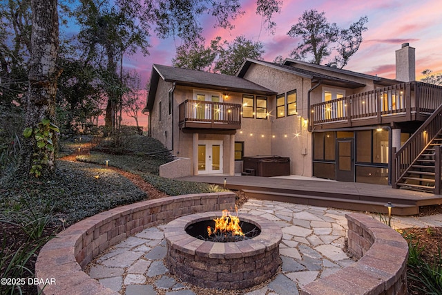 back house at dusk with a hot tub, a patio, a balcony, and an outdoor fire pit