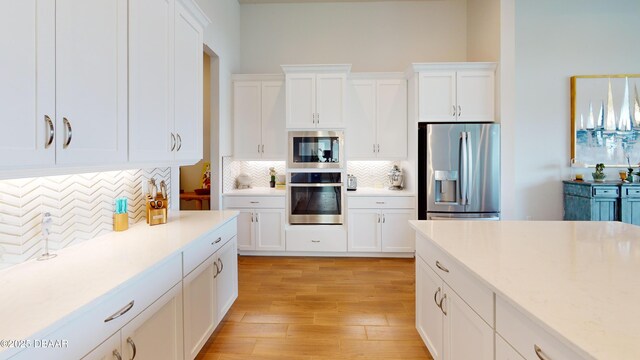 kitchen featuring white cabinets, tasteful backsplash, appliances with stainless steel finishes, and light wood-type flooring