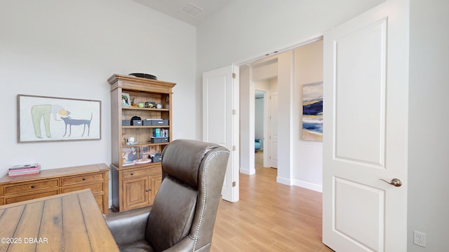 office area with baseboards, light wood finished floors, and visible vents