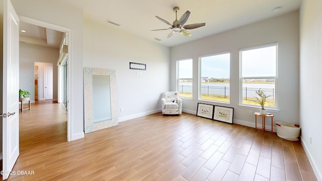 unfurnished room featuring a water view, baseboards, light wood-style floors, visible vents, and a ceiling fan