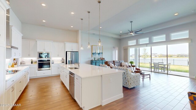 kitchen featuring a towering ceiling, stainless steel appliances, a ceiling fan, a sink, and open floor plan