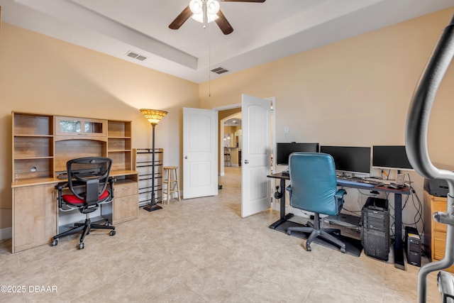office area with a towering ceiling, visible vents, a ceiling fan, and a tray ceiling