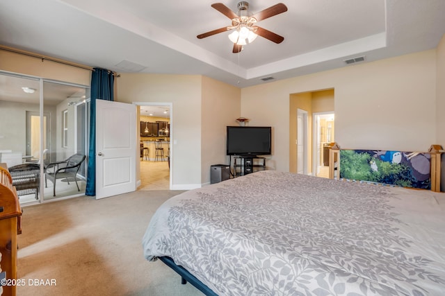bedroom featuring light colored carpet, visible vents, a ceiling fan, and a tray ceiling
