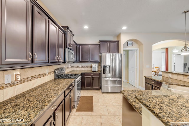 kitchen with arched walkways, decorative backsplash, appliances with stainless steel finishes, dark brown cabinets, and a sink