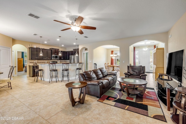 living room featuring light tile patterned flooring, visible vents, a ceiling fan, and arched walkways