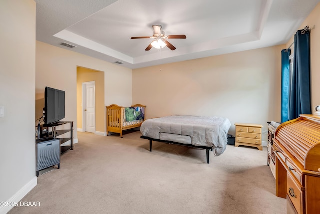 bedroom featuring light carpet, ceiling fan, baseboards, visible vents, and a tray ceiling