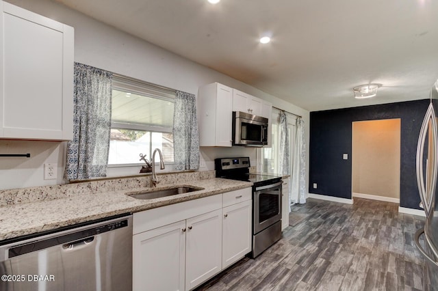 kitchen with dark wood-type flooring, white cabinets, sink, appliances with stainless steel finishes, and light stone counters