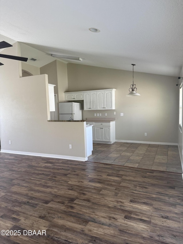 kitchen with pendant lighting, freestanding refrigerator, white cabinetry, vaulted ceiling, and baseboards