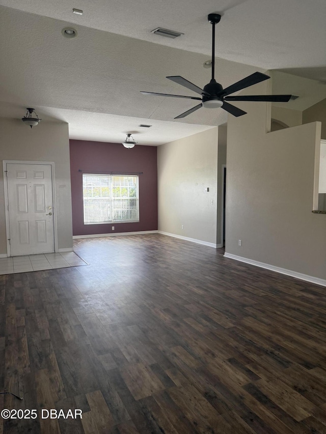 spare room with lofted ceiling, visible vents, baseboards, a ceiling fan, and dark wood-style floors