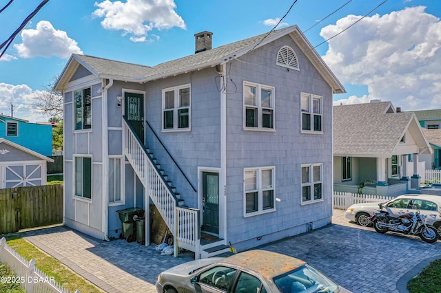 view of front of home with a chimney, stairway, roof with shingles, fence, and a patio area