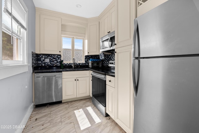 kitchen featuring dark countertops, cream cabinetry, stainless steel appliances, and a sink