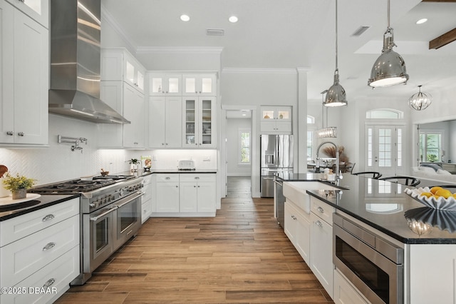 3236 Modena Way, New Smyrna Beach, FL 32168 - kitchen with stainless steel appliances, wall chimney range hood, dark countertops, crown molding, and light wood-style flooring