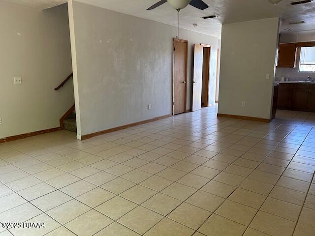 unfurnished living room featuring stairs, light tile patterned floors, a ceiling fan, and baseboards