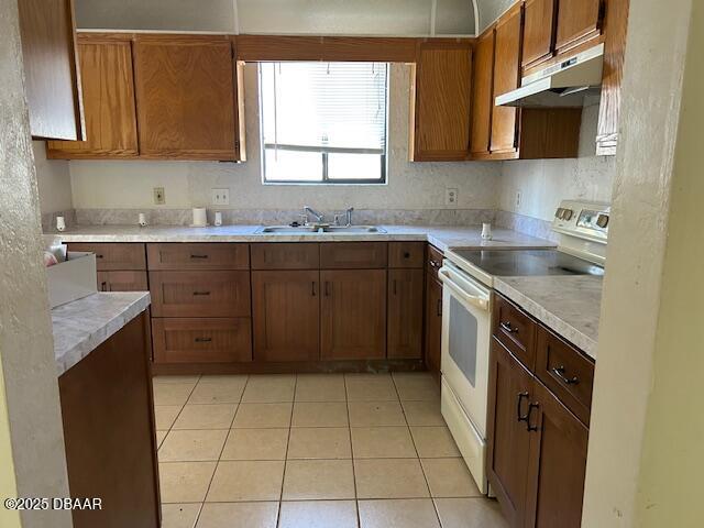 kitchen with white range with electric cooktop, under cabinet range hood, a sink, light countertops, and light tile patterned floors