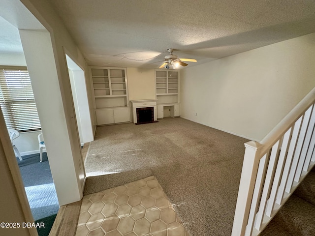 unfurnished living room featuring built in shelves, carpet, a ceiling fan, a textured ceiling, and a brick fireplace