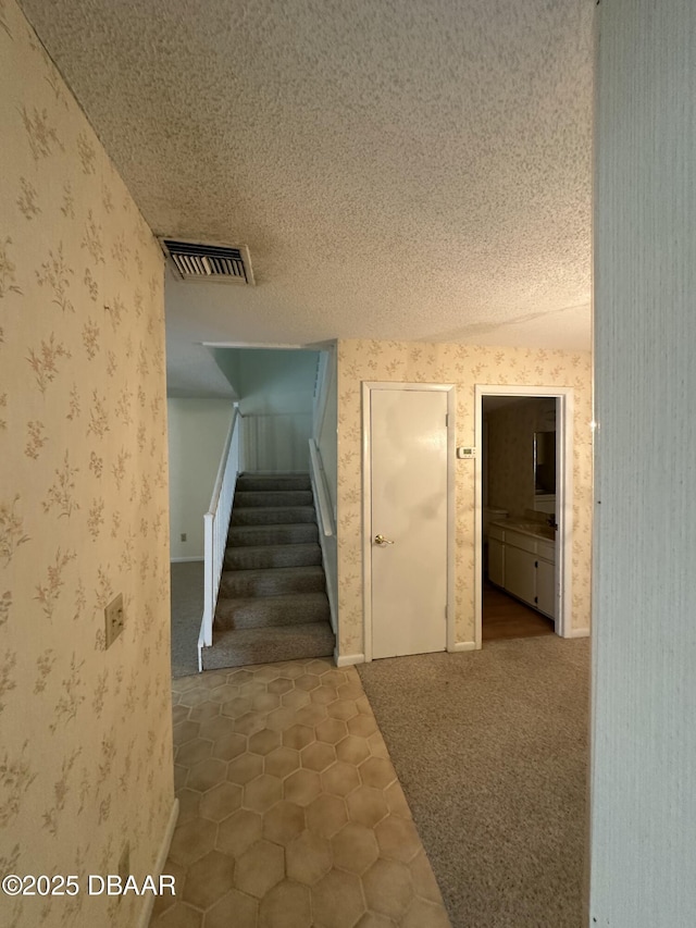 staircase with visible vents, carpet floors, wallpapered walls, a textured ceiling, and tile patterned floors