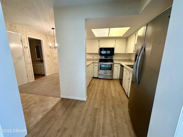 kitchen featuring light wood finished floors, stainless steel appliances, white cabinets, wallpapered walls, and light countertops