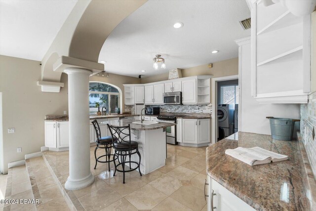 kitchen featuring a kitchen breakfast bar, stainless steel appliances, decorative columns, an island with sink, and white cabinets