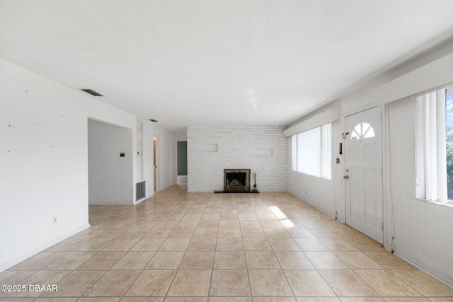 unfurnished living room with light tile patterned floors, a textured ceiling, and a brick fireplace