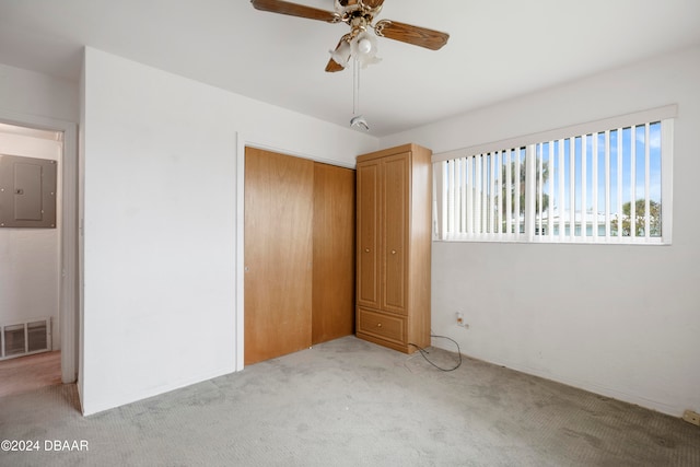 unfurnished bedroom with light carpet, electric panel, a closet, and ceiling fan