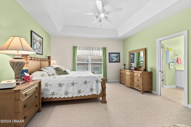 bedroom with a raised ceiling, light carpet, ceiling fan, and connected bathroom