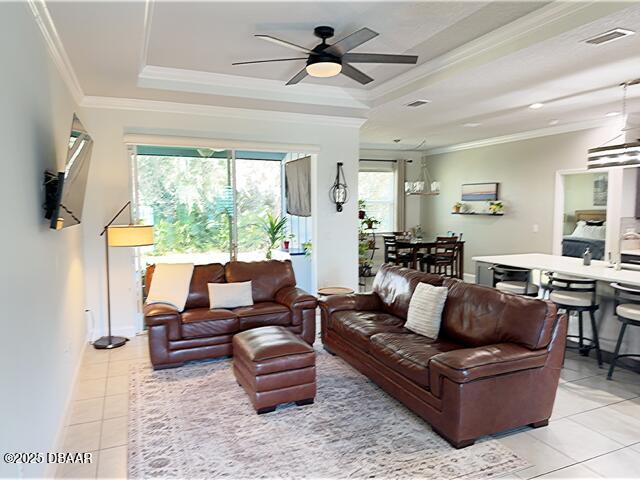 living room featuring crown molding, light tile patterned floors, a tray ceiling, and ceiling fan