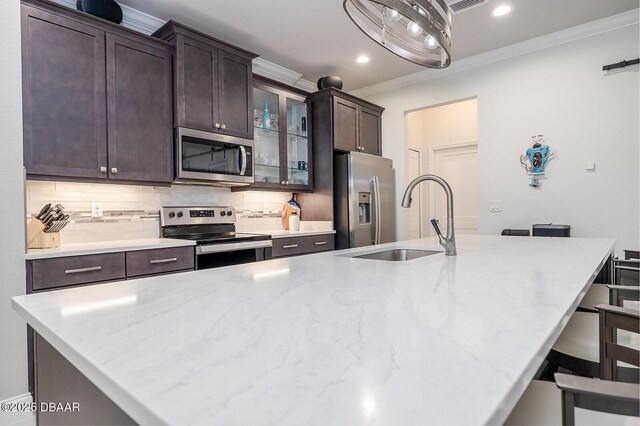 1321 Tullamore Blvd, Ormond Beach, FL 32174 - kitchen with crown molding, a kitchen island with sink, dark brown cabinetry, light countertops, and appliances with stainless steel finishes