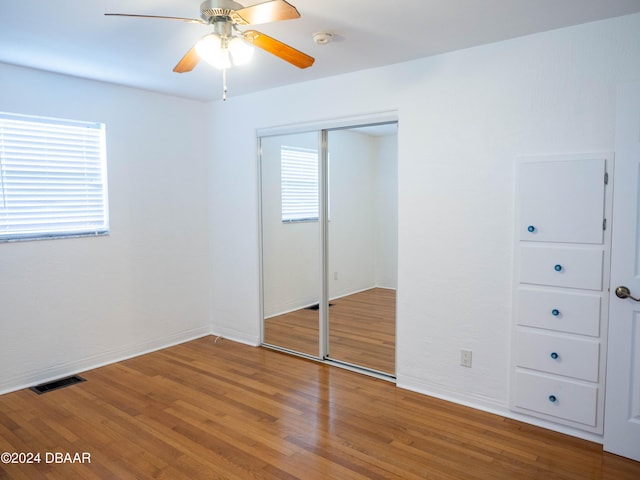 unfurnished bedroom with multiple windows, ceiling fan, a closet, and hardwood / wood-style flooring