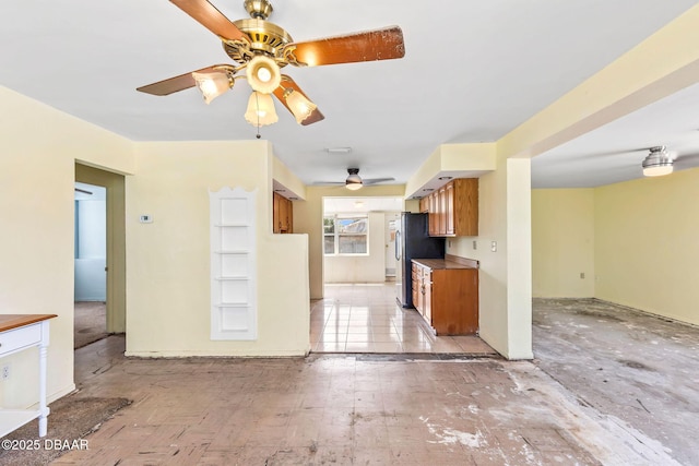 kitchen featuring a ceiling fan, freestanding refrigerator, and brown cabinets