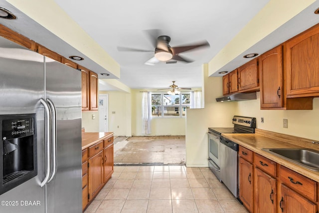 kitchen featuring stainless steel appliances, brown cabinetry, a ceiling fan, a sink, and under cabinet range hood