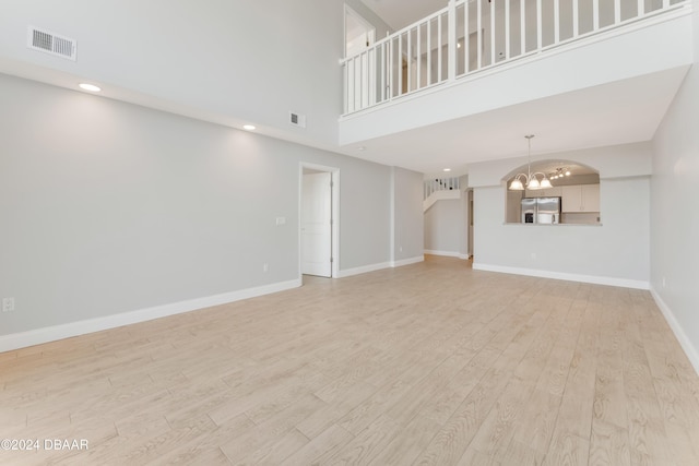 unfurnished living room with an inviting chandelier, a high ceiling, and light hardwood / wood-style flooring