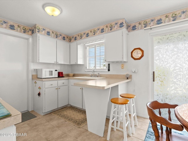 kitchen with kitchen peninsula, light tile patterned flooring, white cabinets, and a breakfast bar