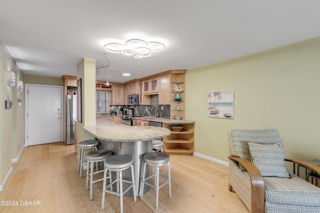 kitchen with a kitchen breakfast bar, decorative backsplash, stainless steel appliances, and light hardwood / wood-style floors