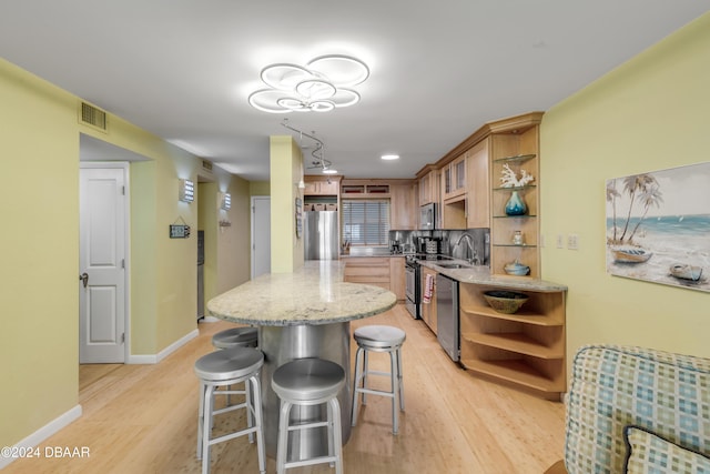 kitchen featuring decorative backsplash, a kitchen bar, light stone counters, stainless steel appliances, and light hardwood / wood-style flooring