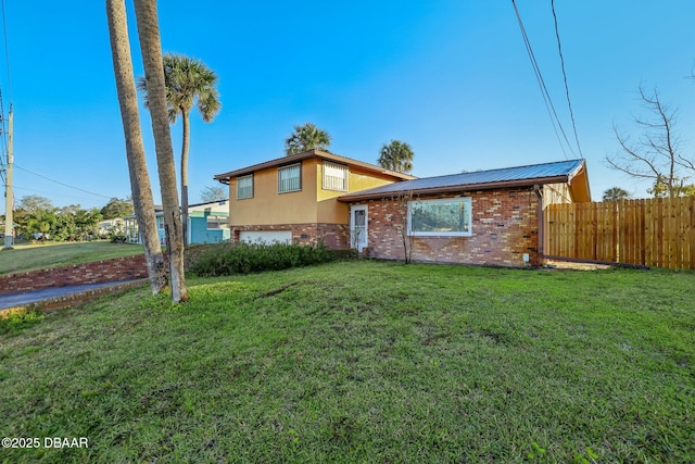 tri-level home featuring fence, an attached garage, stucco siding, a front lawn, and brick siding