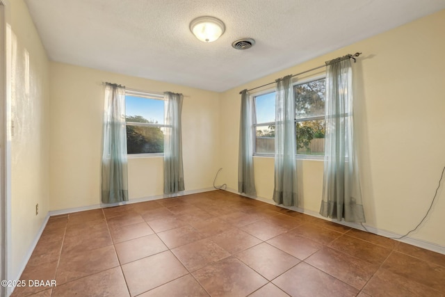 spare room with tile patterned floors, visible vents, a textured ceiling, and baseboards