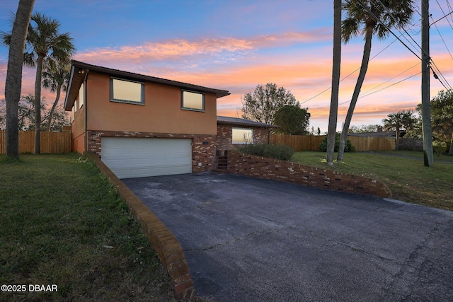 property exterior at dusk with aphalt driveway, fence, a garage, and stucco siding