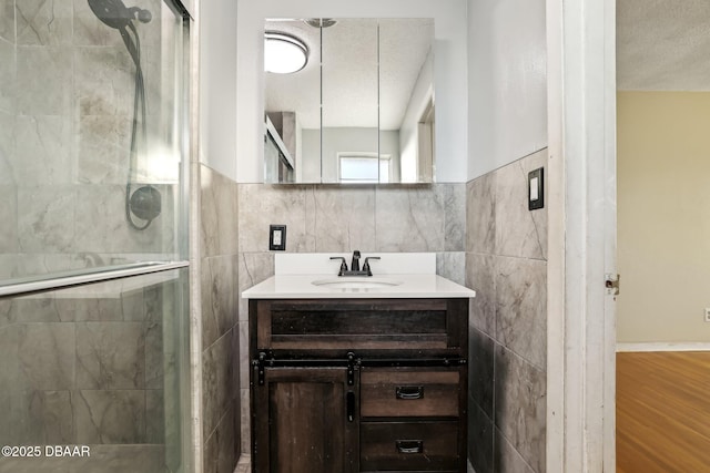 bathroom with a shower stall, tile walls, vanity, wood finished floors, and a textured ceiling