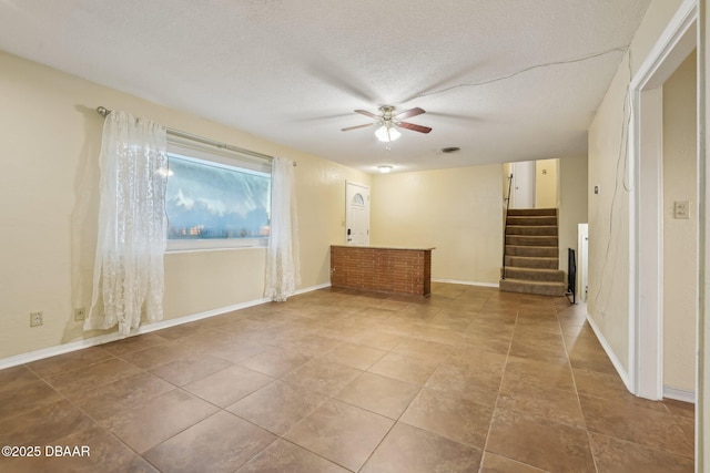 empty room featuring baseboards, stairway, a textured ceiling, and ceiling fan