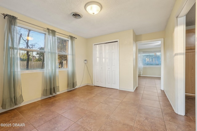 unfurnished bedroom with visible vents, baseboards, light tile patterned floors, a closet, and a textured ceiling