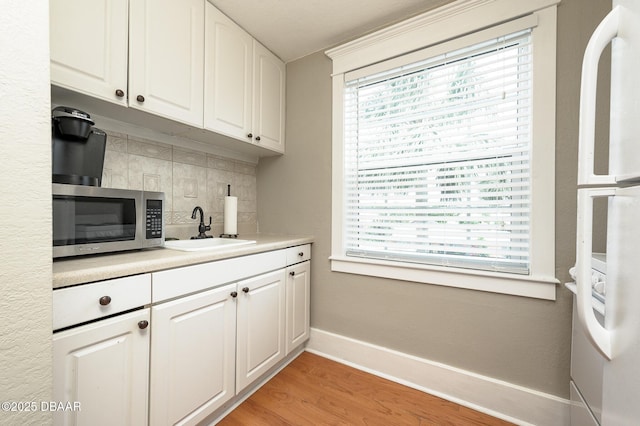 kitchen featuring white fridge, white cabinets, sink, light hardwood / wood-style flooring, and tasteful backsplash