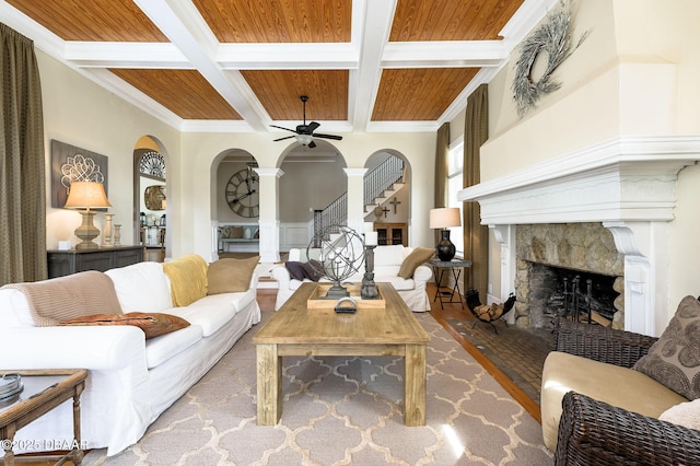 living room featuring beamed ceiling, crown molding, wooden ceiling, coffered ceiling, and a stone fireplace