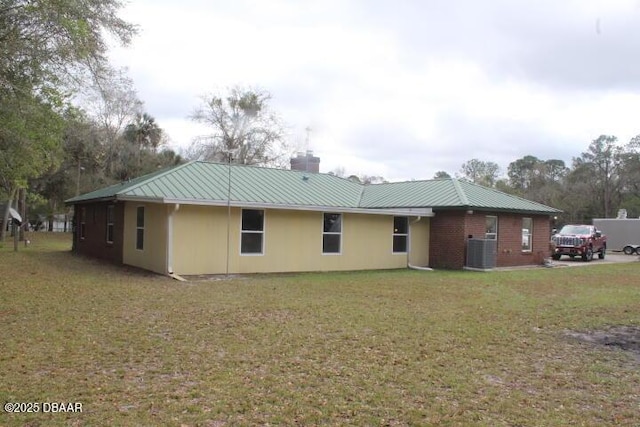 back of property featuring metal roof, a yard, a chimney, and central air condition unit