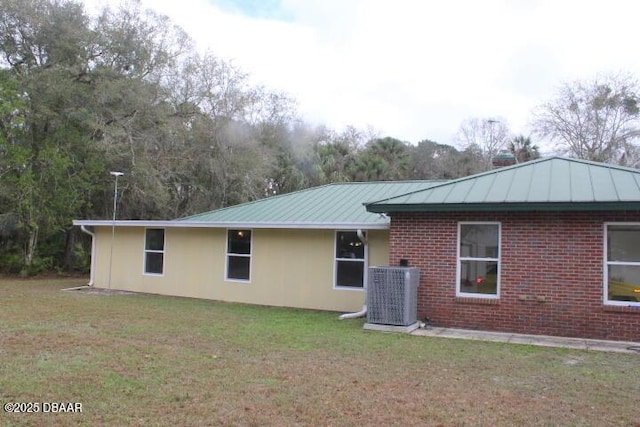 rear view of house with metal roof, central AC, brick siding, and a lawn