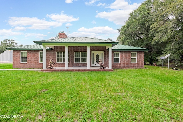 rear view of property with metal roof, brick siding, a lawn, a standing seam roof, and a chimney