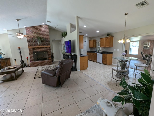 living area featuring light tile patterned floors, visible vents, a brick fireplace, vaulted ceiling, and ceiling fan with notable chandelier